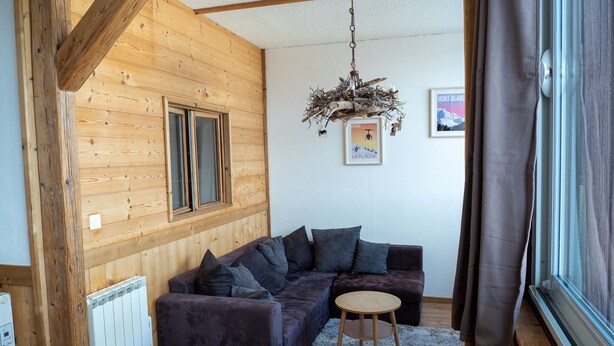 A cozy room with a wooden ceiling, a dark purple sofa, a small round table, and a unique chandelier.