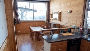 A wooden interior with a dining area, kitchen, and large window with a view of mountains.