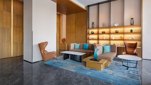 Un lobby moderno con un conjunto de sofás, dos sillones, una mesa de centro y una estantería decorativa con objetos.