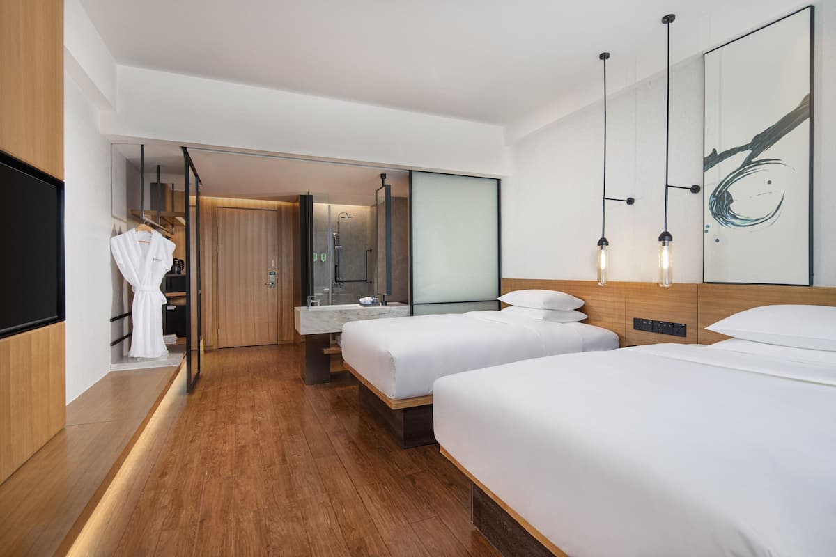 A modern hotel room with two beds, a large mirror, a wooden floor, and a robe hanging on the wall.