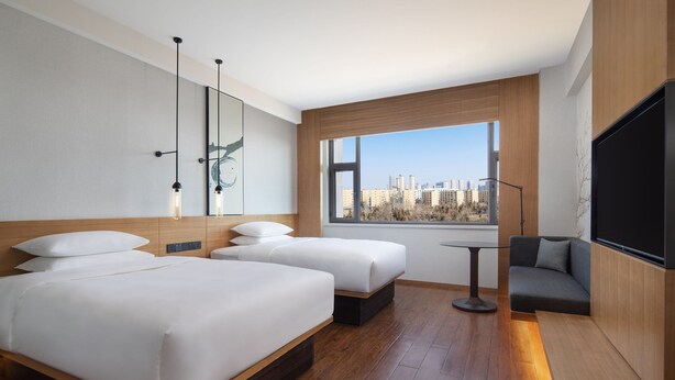 Una habitación de hotel moderna con dos camas, un sofá, un televisor y un ventanal con vistas a la ciudad.