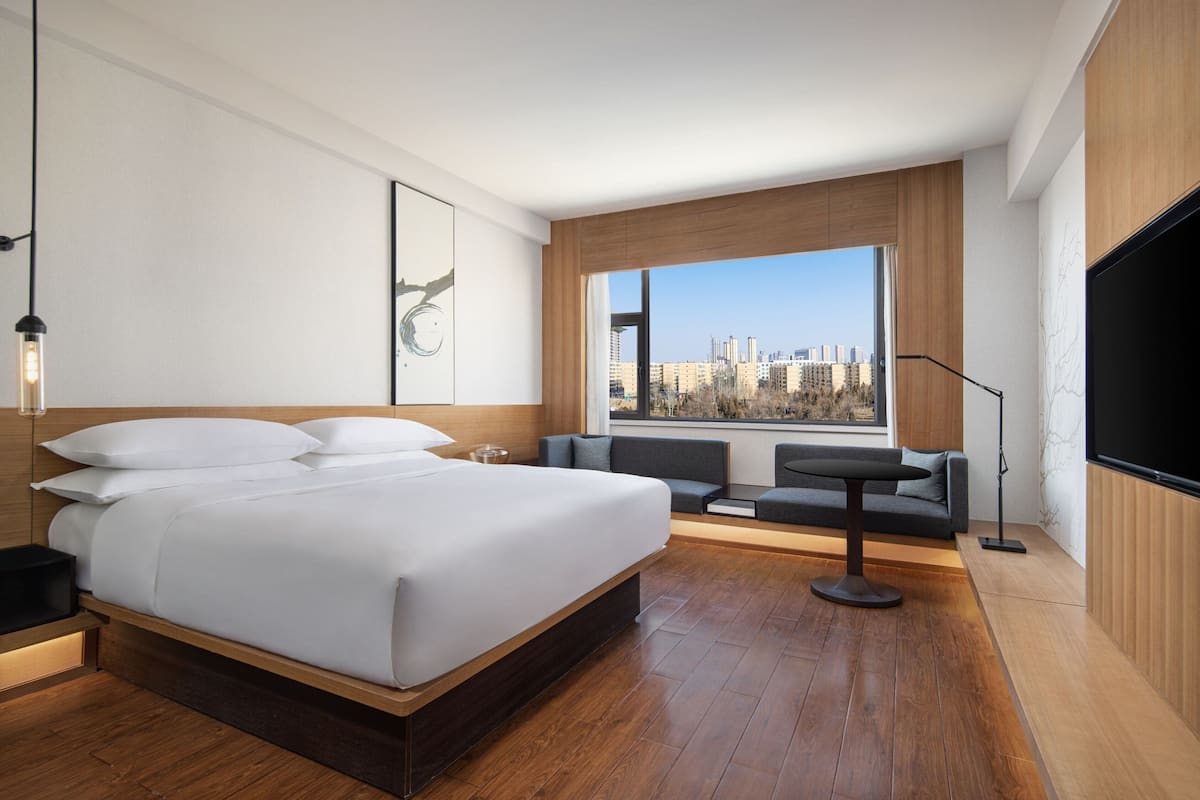 A modern hotel room with a large bed, a seating area with a view of the city, and a flat-screen TV.