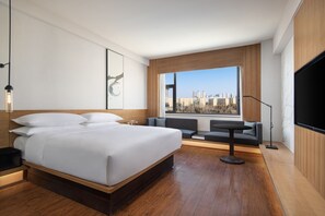 Ett modernt hotellrum med en stor säng, en sittgrupp med utsikt över staden och en platt-TV.