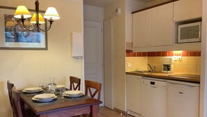 A dining table set with plates and glasses, a chandelier, and a kitchen with white cabinets and a microwave. - Apartment Basque Country Saint Jean Pied de Port (Uhart cize)