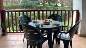 A covered patio with a round table and chairs, a breakfast setting with croissants and juice, and a view of a garden and trees. - Apartment Basque Country Saint Jean Pied de Port (Uhart cize)