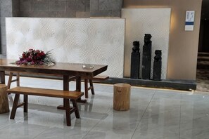 A wooden table with benches, a patterned wall, and two black statues. - Poli Garden Hotel (Qianwei County)