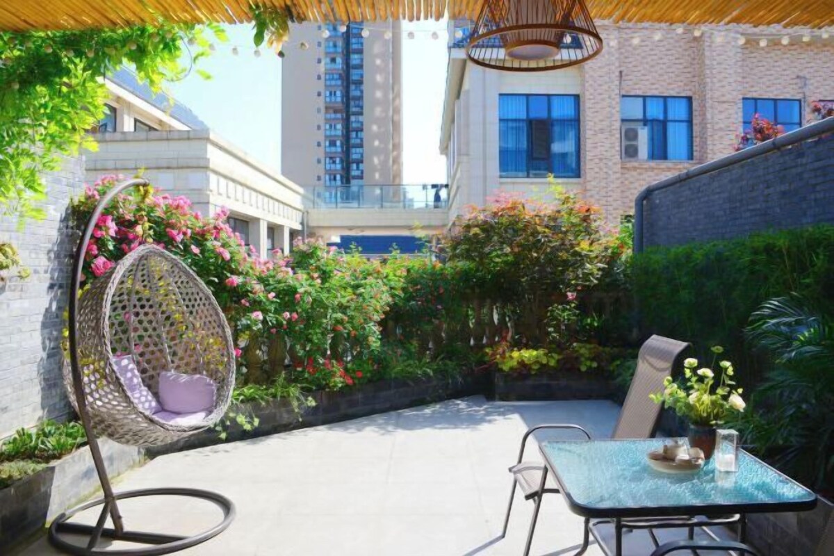 A patio with a hanging chair, a table, and a potted plant.
