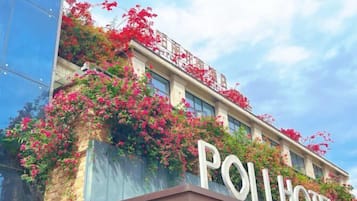A hotel with a prominent 'POLHOTEL' sign, a brick facade, and red flowering vines.