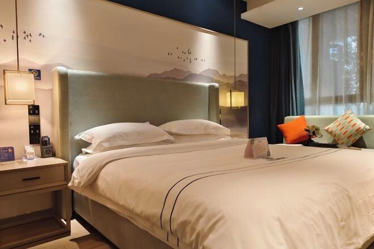 A hotel room with a large bed, bedside tables, a nightstand, a lamp, and a view of the outdoors.