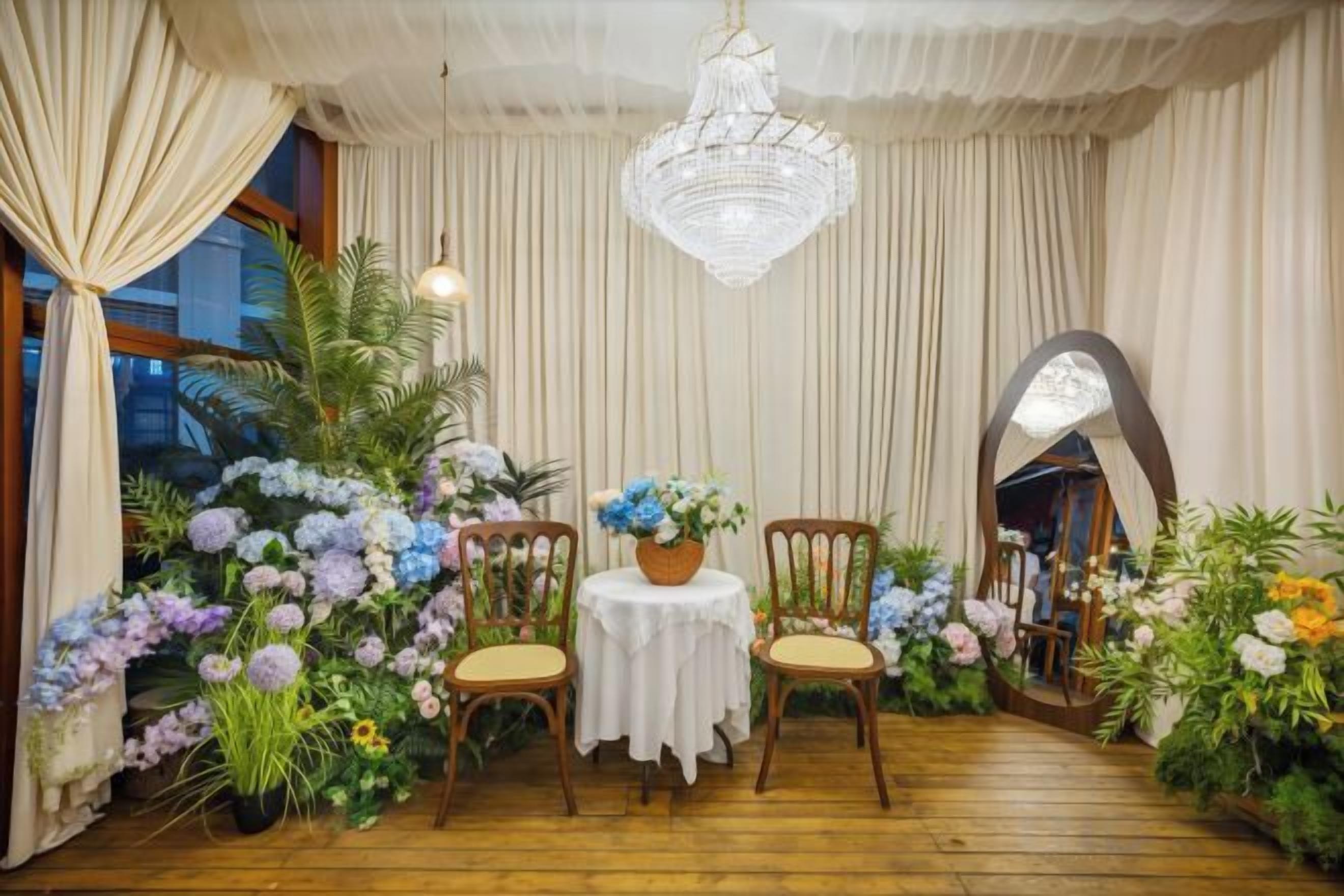 Una habitación con piso de madera, dos sillas, una mesa con mantel blanco y un candelabro.