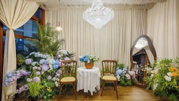 Una habitación con piso de madera, dos sillas, una mesa con mantel blanco y un candelabro.
