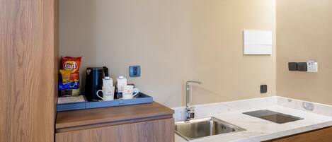 A modern kitchen with wooden cabinets, a marble countertop, a double sink, and a coffee station with a kettle and cups.