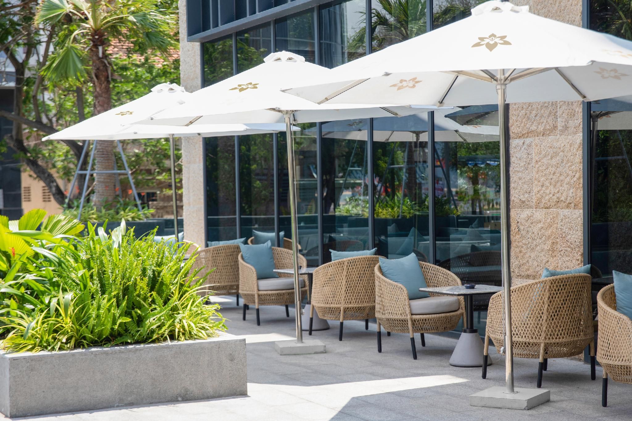 Outdoor seating with wicker chairs and white umbrellas, surrounded by greenery and modern architecture.