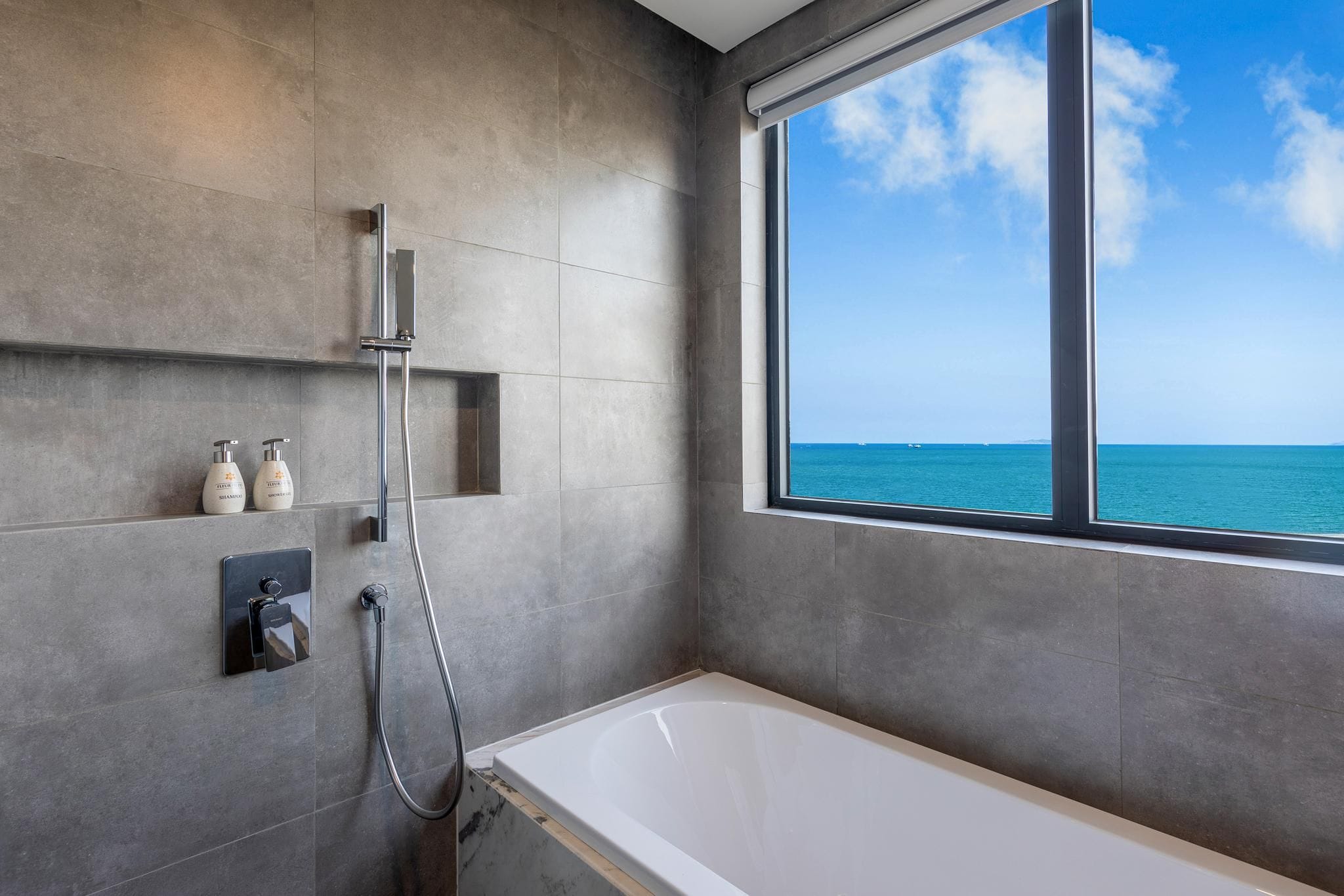 Ein modernes Badezimmer mit Badewanne, Dusche und einem Fenster mit Blick aufs Meer.