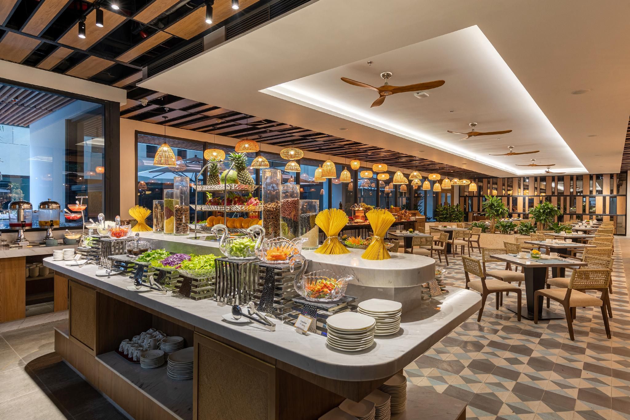 A modern hotel lobby with a buffet area, seating arrangements, and a ceiling fan.