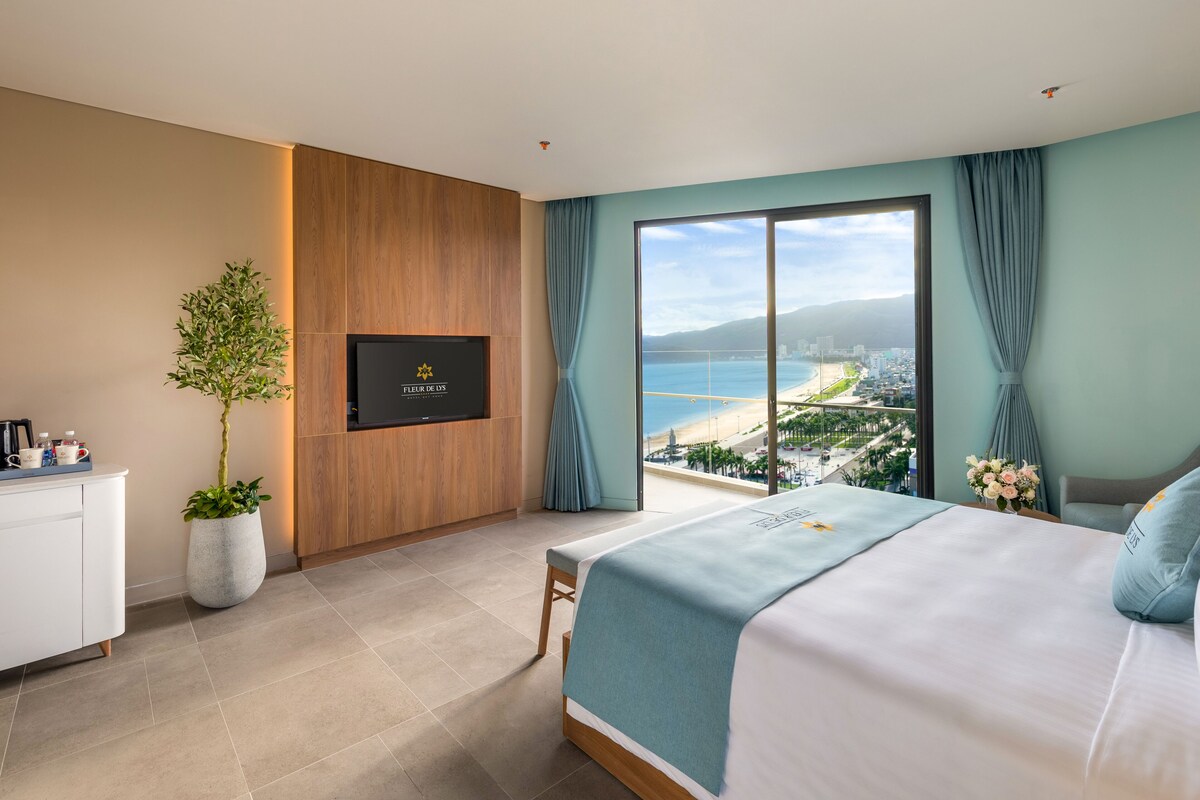 Ein Hotelzimmer mit Bett, Fernseher, Pflanze und Blick auf den Strand.