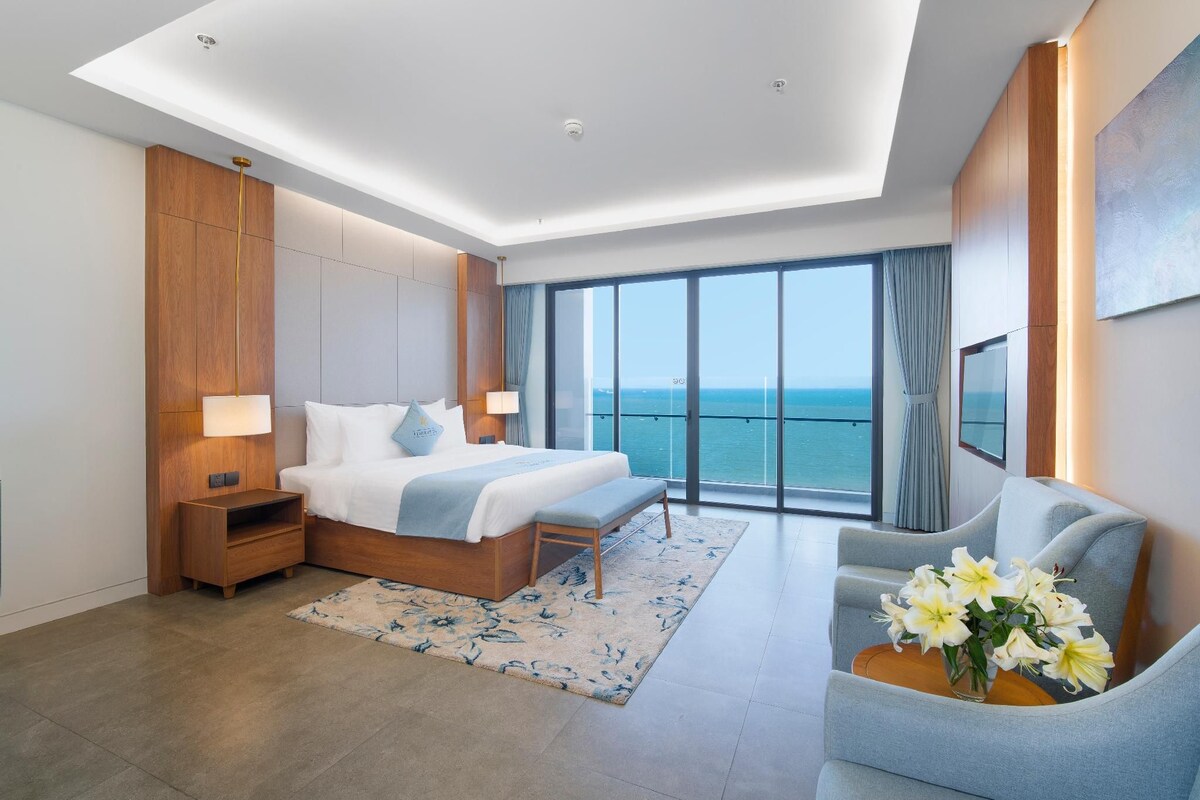 Ein modernes Hotelzimmer mit einem großen Bett, einer Sitzecke und Blick auf das Meer.