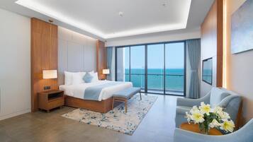 A modern hotel room with a large bed, a seating area, and a view of the sea.