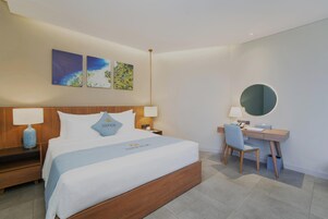 Habitación de hotel con cama, mesitas de noche, escritorio, una silla, un espejo redondo y decoración en la pared.