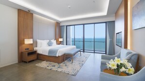 Une chambre d’hôtel moderne dotée d’un grand lit, d’un coin salon et offrant une vue sur l’océan.
