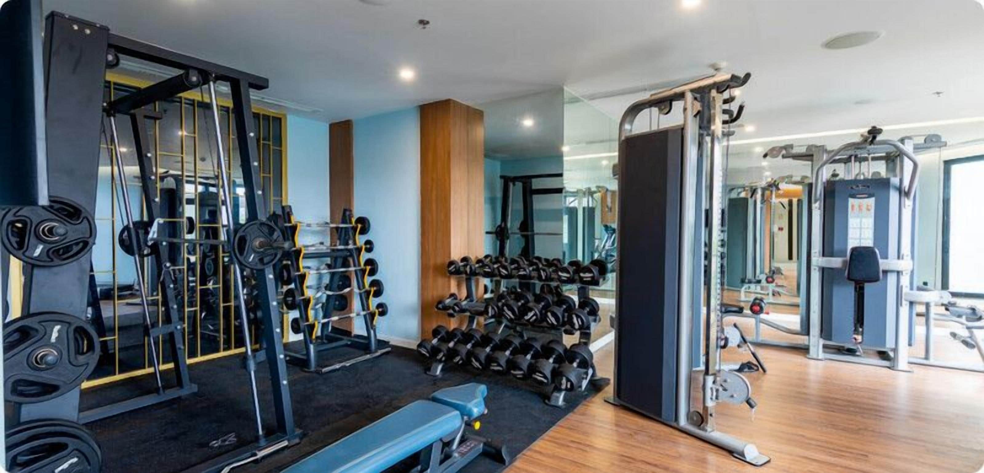 A gym with weightlifting equipment, dumbbells, and a bench.