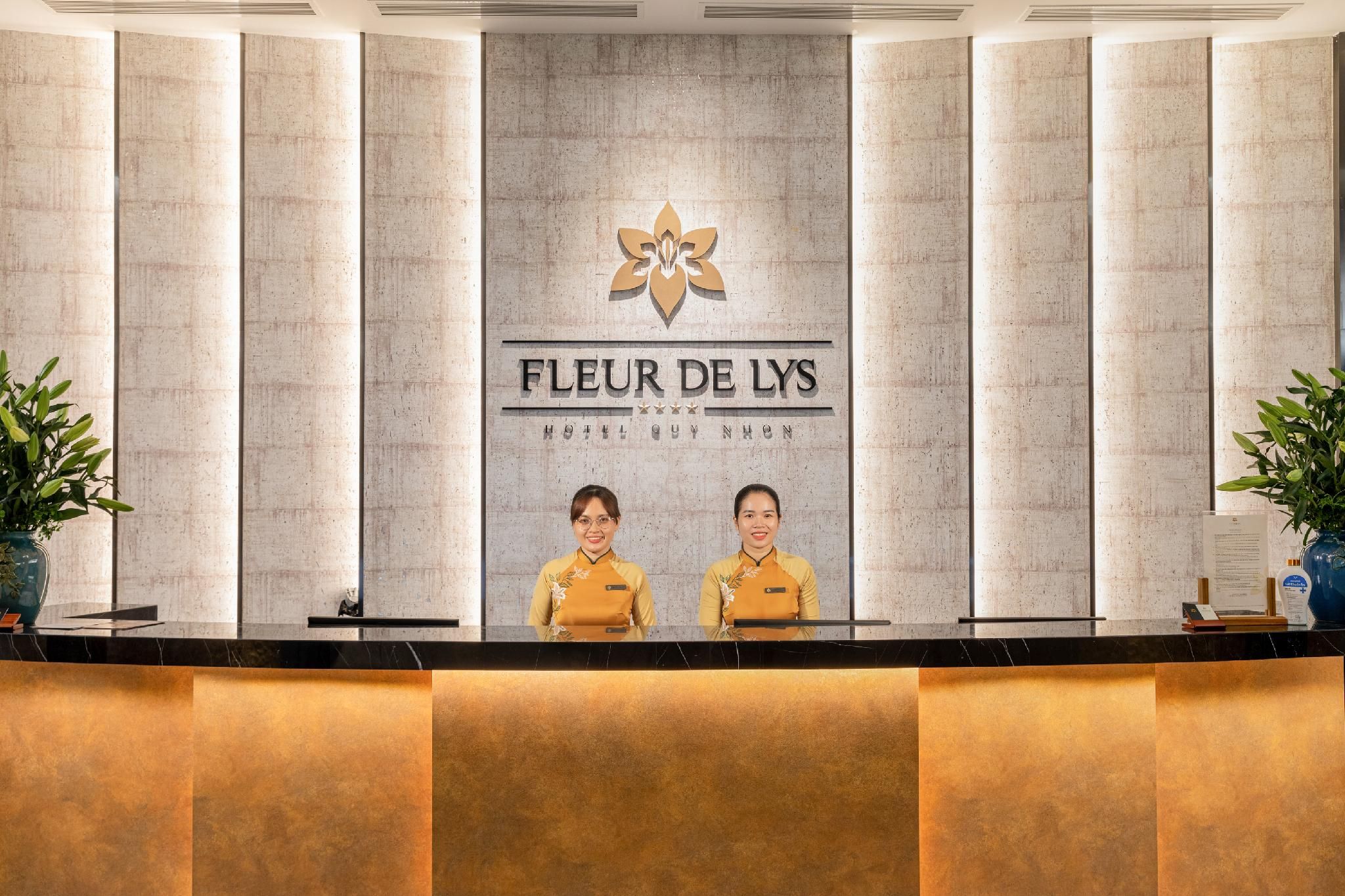 Un mostrador de recepción de hotel con el logotipo y el nombre 'FLEUR DE LYS' sobre dos empleados.