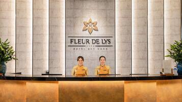 Un mostrador de recepción de hotel con el logotipo y el nombre 'FLEUR DE LYS' sobre dos empleados.