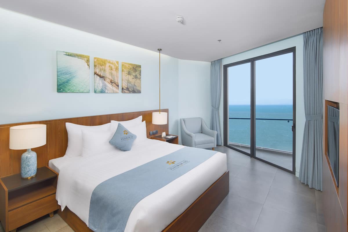 Habitación de hotel con una cama grande, una silla, una mesita de noche y vista al océano.