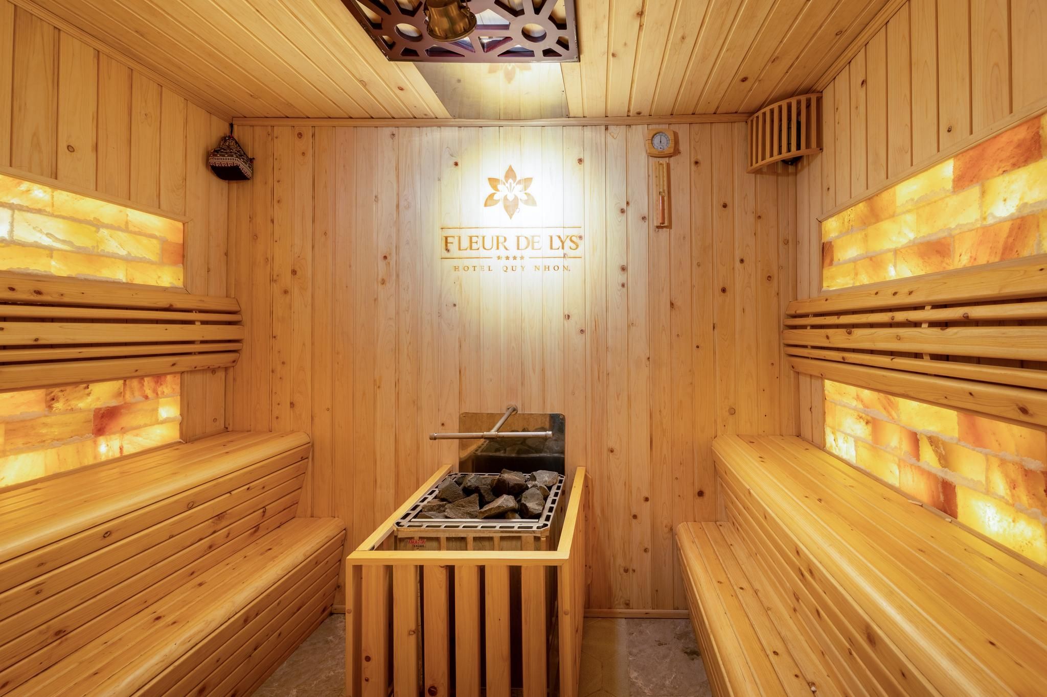 Un sauna en bois, doté de bancs, d’un système de chauffage central et d’un logo sur le mur.