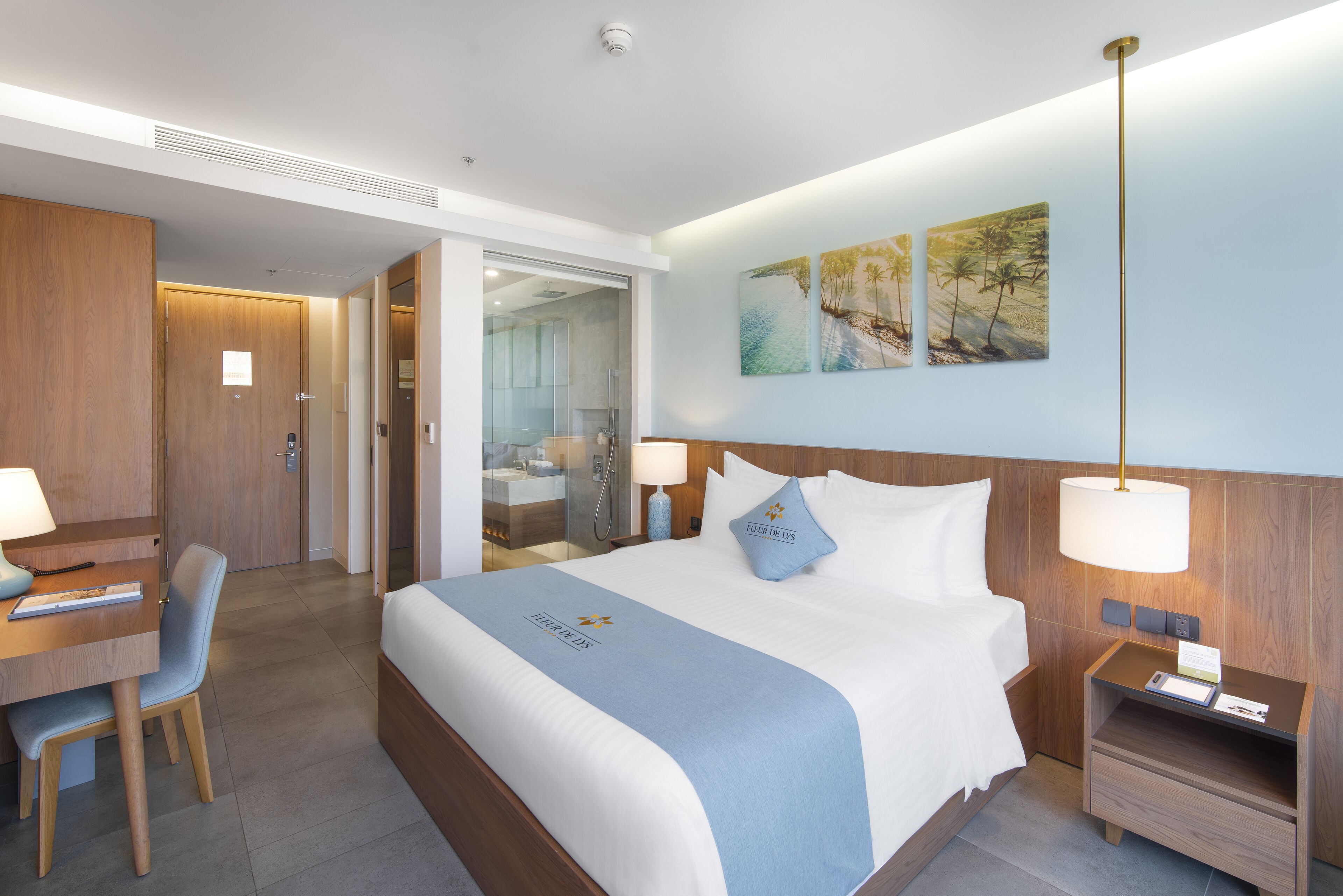 Une chambre d’hôtel avec un lit, un bureau et une chaise. On peut apercevoir la salle de bain à travers une porte en verre.