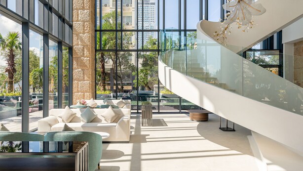 Un intérieur moderne avec un escalier en verre, un espace extérieur aménagé et de grandes fenêtres offrant une vue sur la ville.