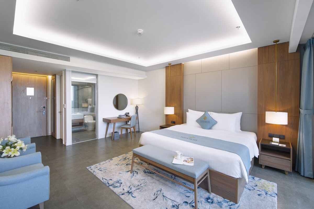 A modern hotel room with a large bed, bedside tables, a desk, and a seating area.