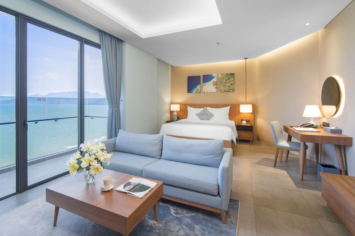 Una habitación de hotel moderna con un balcón amplio, una cama, un escritorio y un sofá.