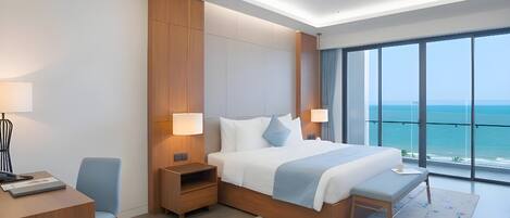 A modern hotel room with a large bed, bedside tables, a desk, and a view of the ocean.