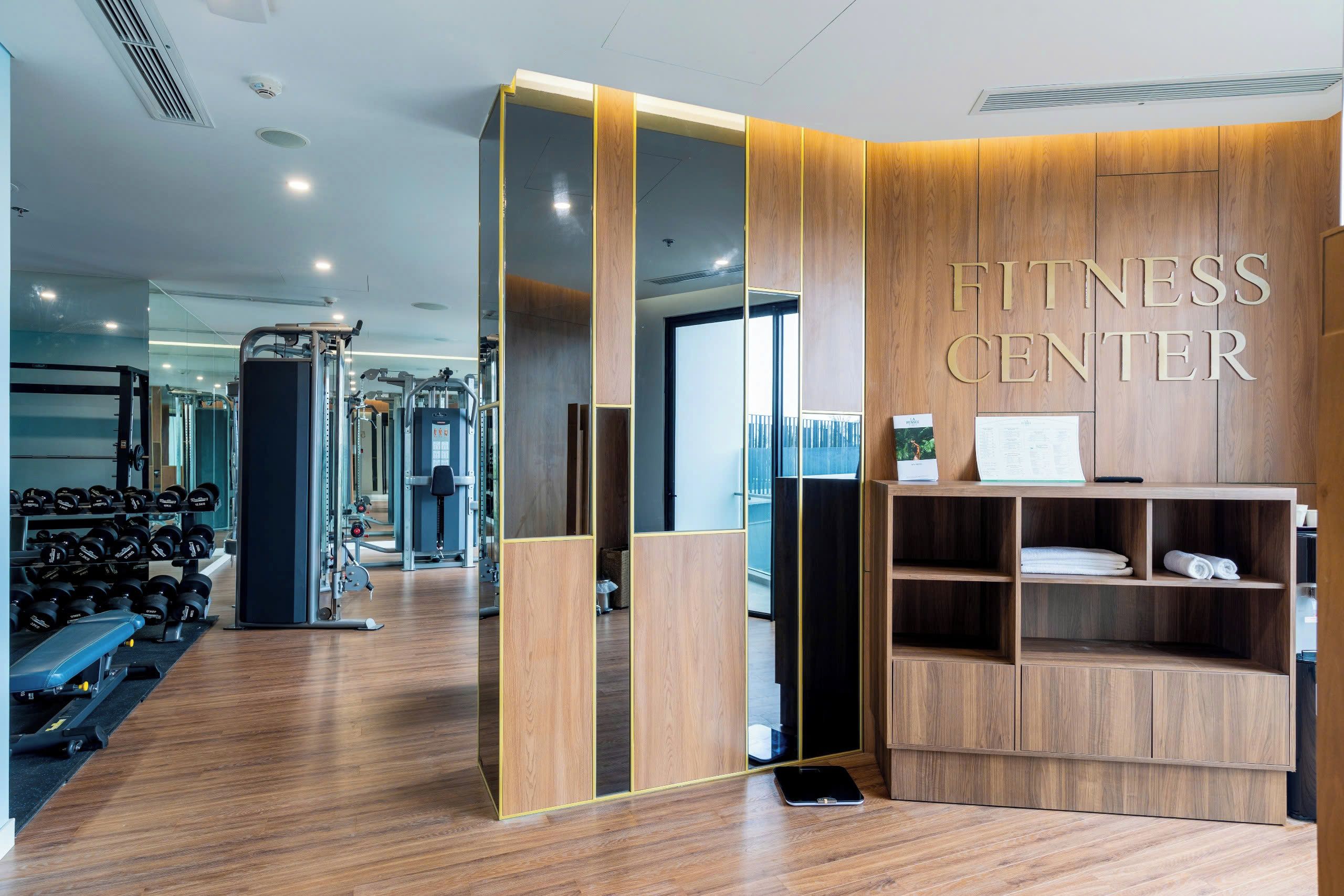 Et fitnesscenter med træningsudstyr, en receptionsdisk og et område med trægulv.