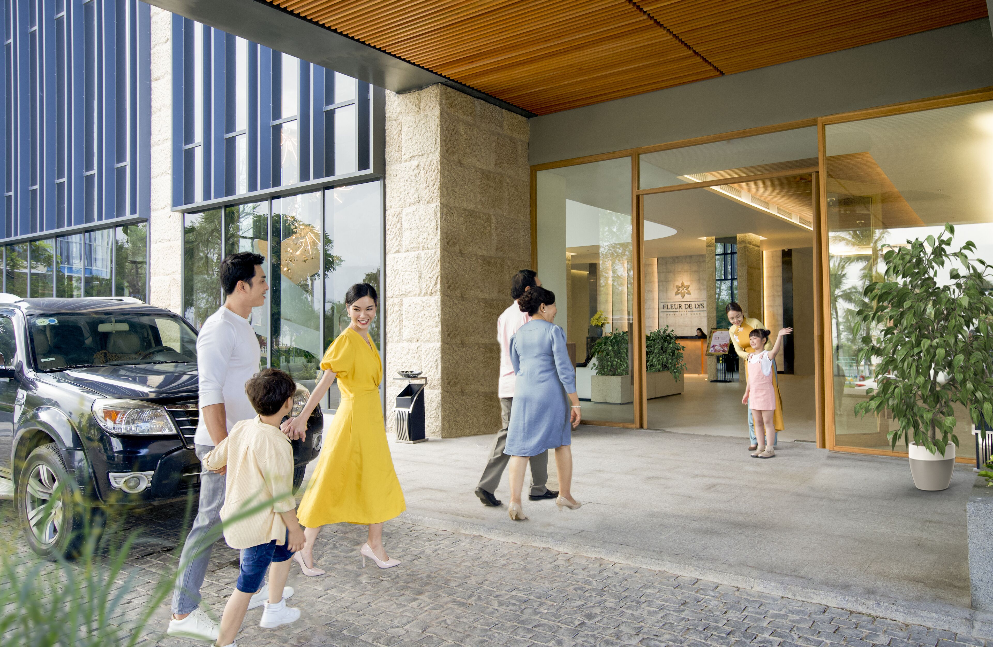 A family walking towards a hotel entrance with a modern design, large windows, and a stone facade.