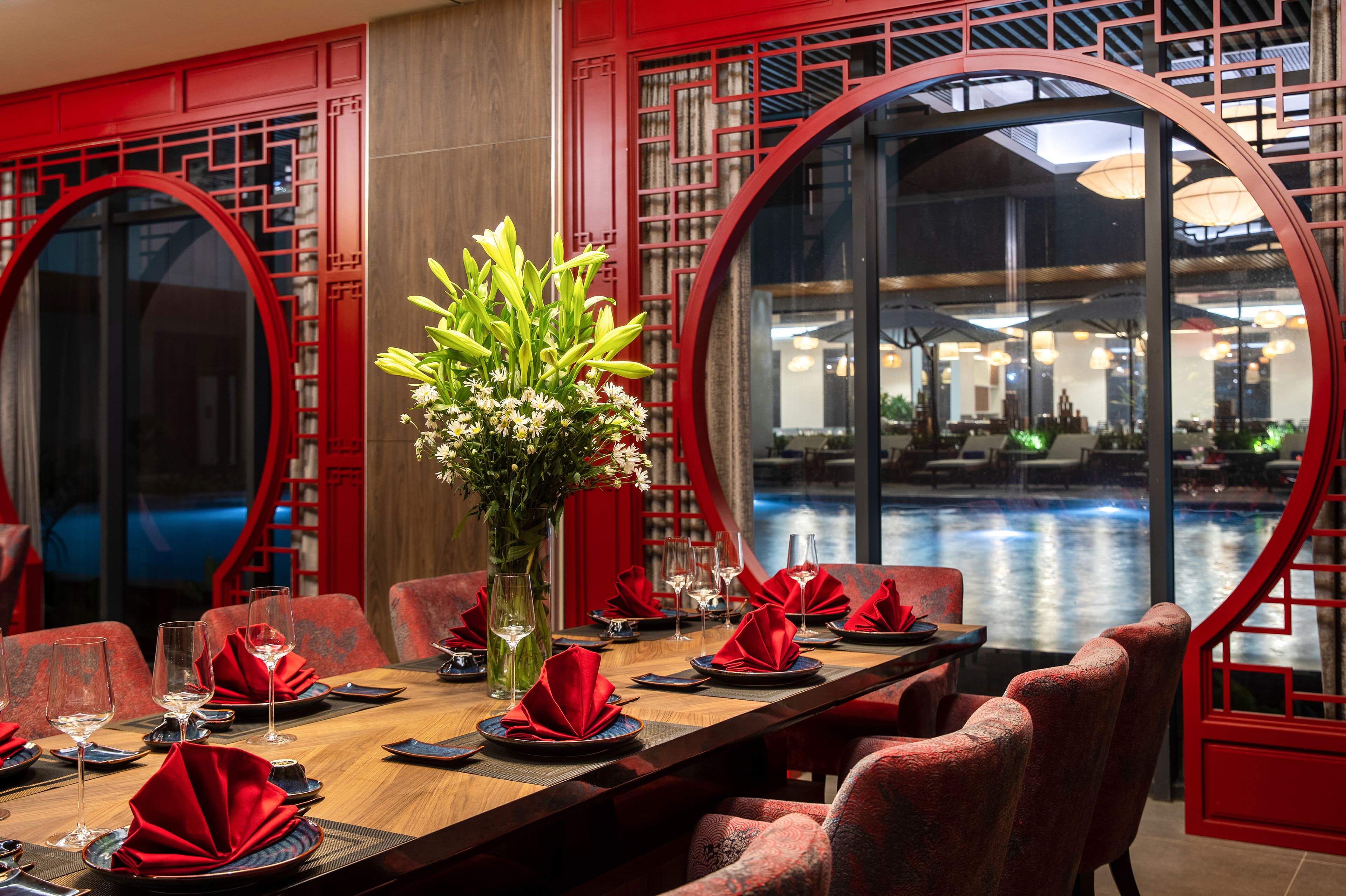 Un comedor con decoración roja, un jarrón con flores y vistas a un cuerpo de agua.