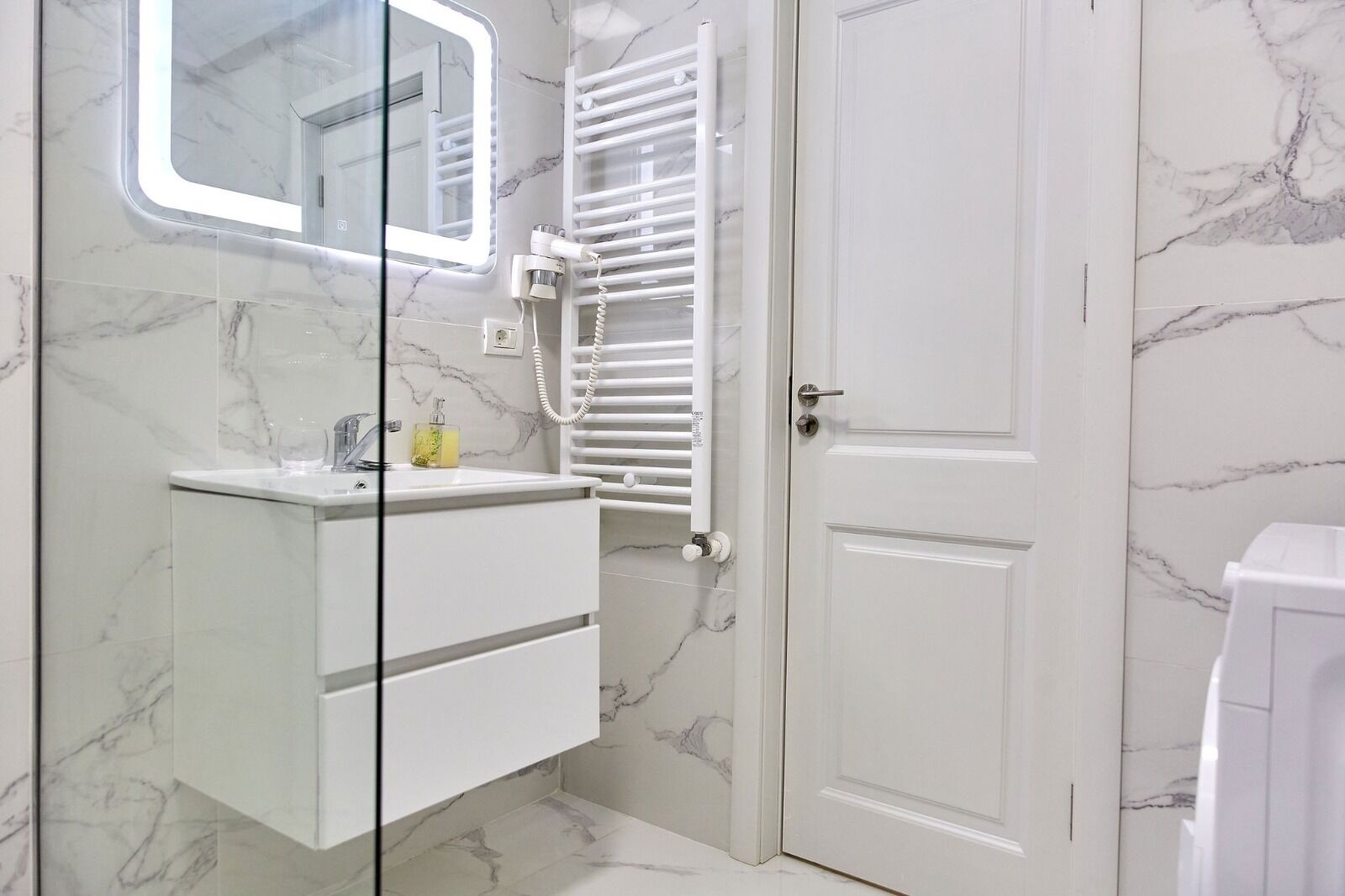 A bathroom with a marble floor, a white vanity with a mirror, a towel rack, and a door.