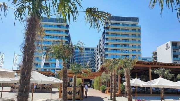 Ein Hotelbereich direkt am Strand, mit Palmen, Liegestühlen und einer Holzterrasse.