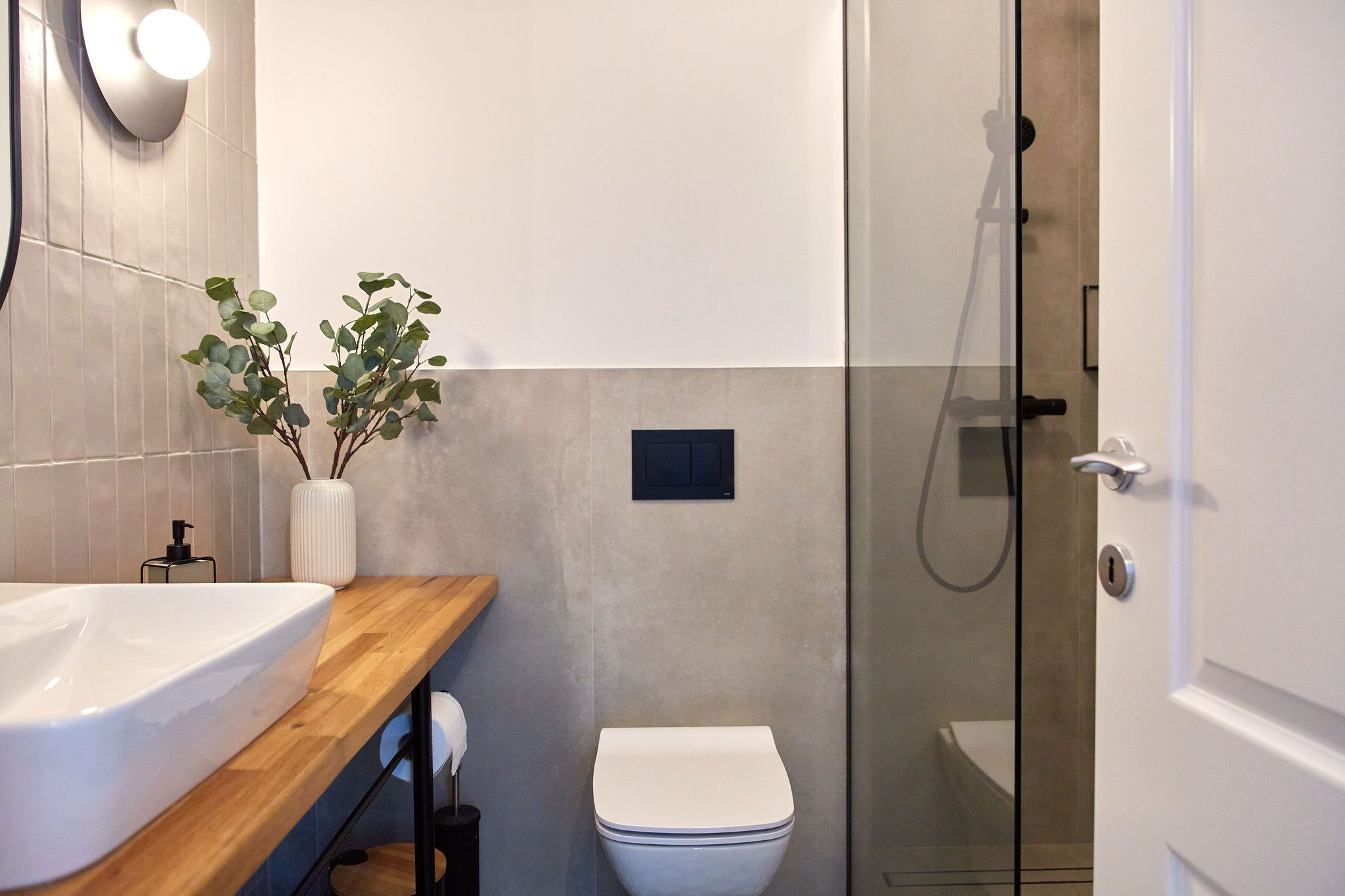 Een moderne badkamer met een houten wastafelmeubel, een witte wastafel, een toilet en een douchecabine met glazen wanden.
