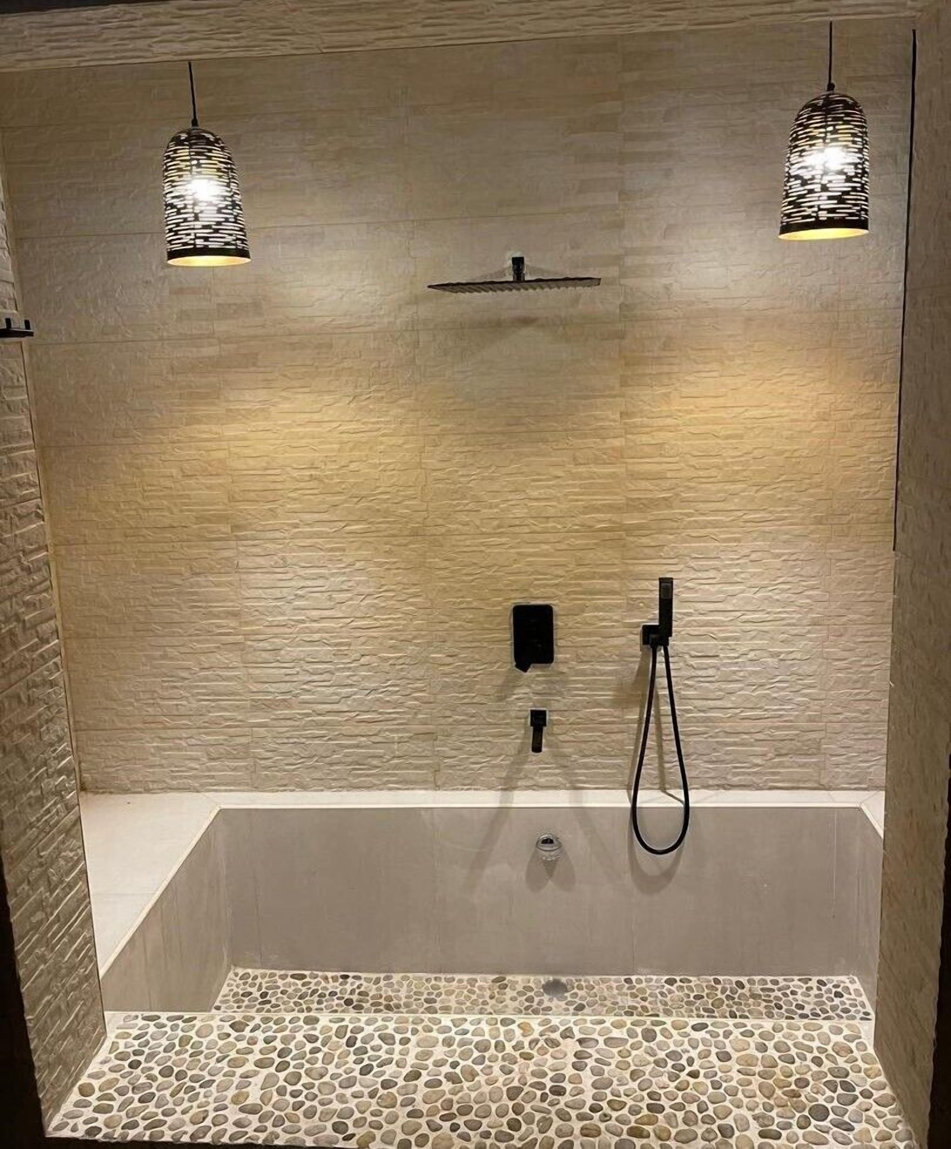 A modern bathroom with a stone-textured wall, a freestanding bathtub, and two pendant lights.