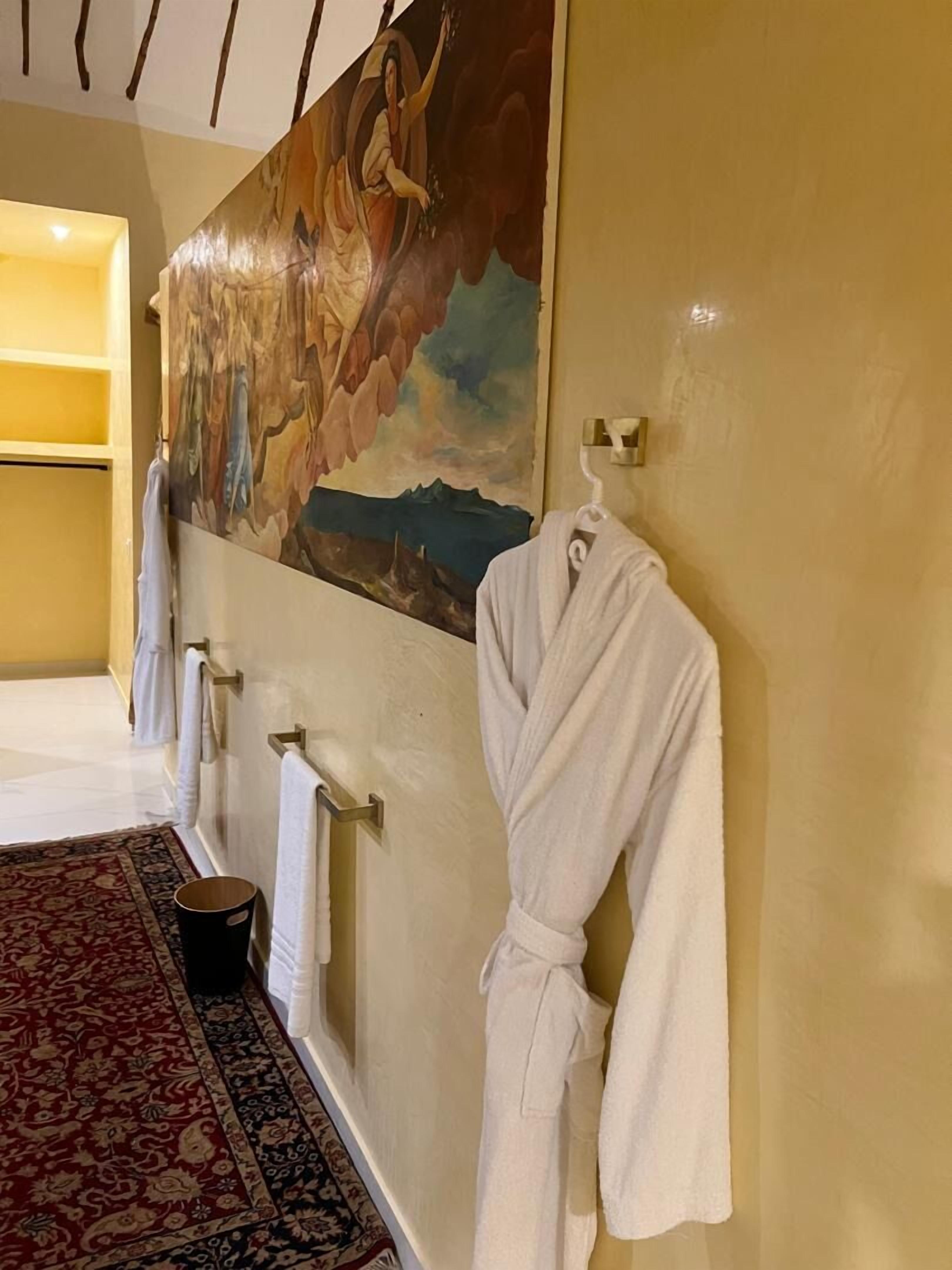 Um corredor com uma pintura grande, um roupão branco pendurado e um tapete estampado.