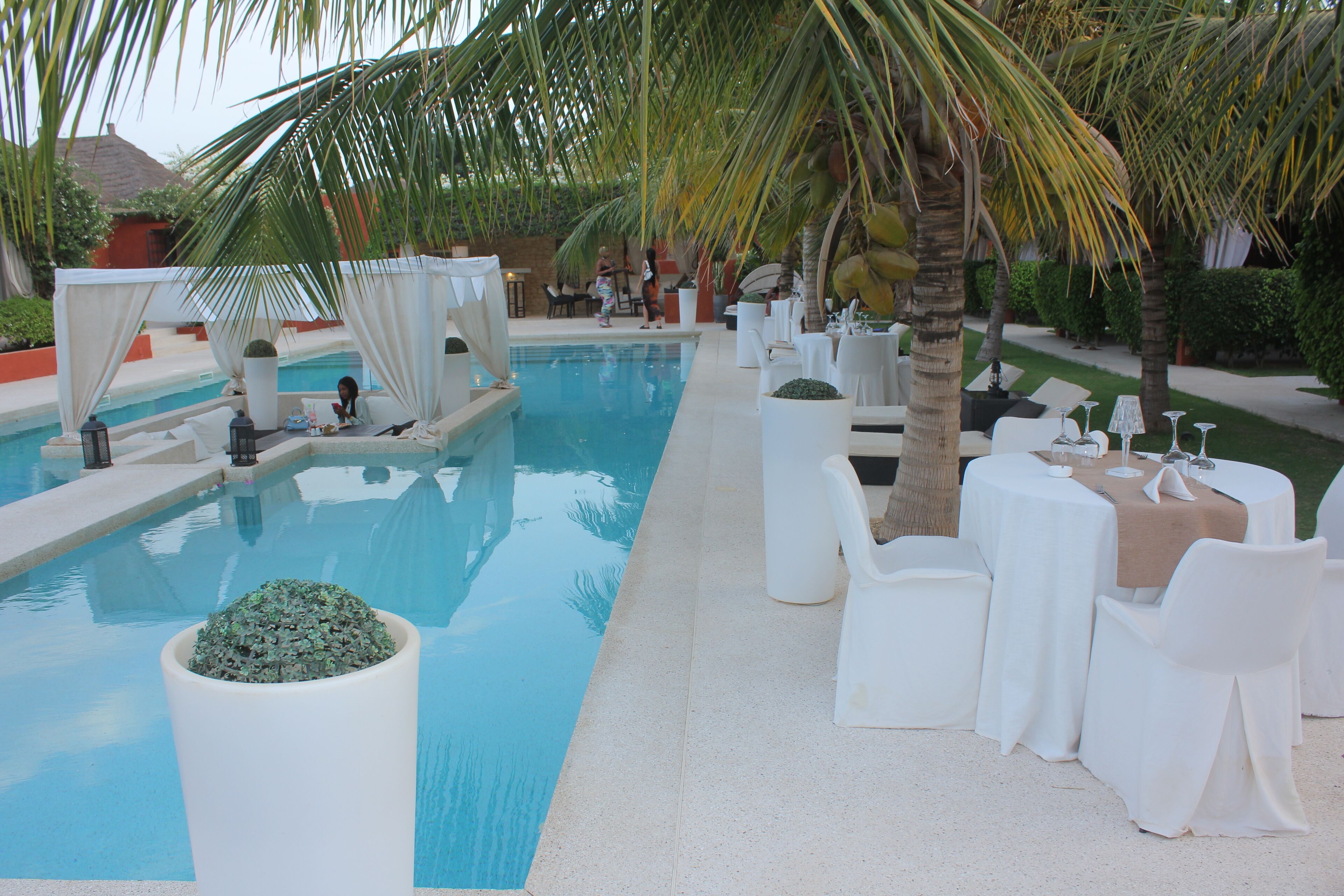 A poolside area with a clear pool, white lounge chairs, and tables set for dining.