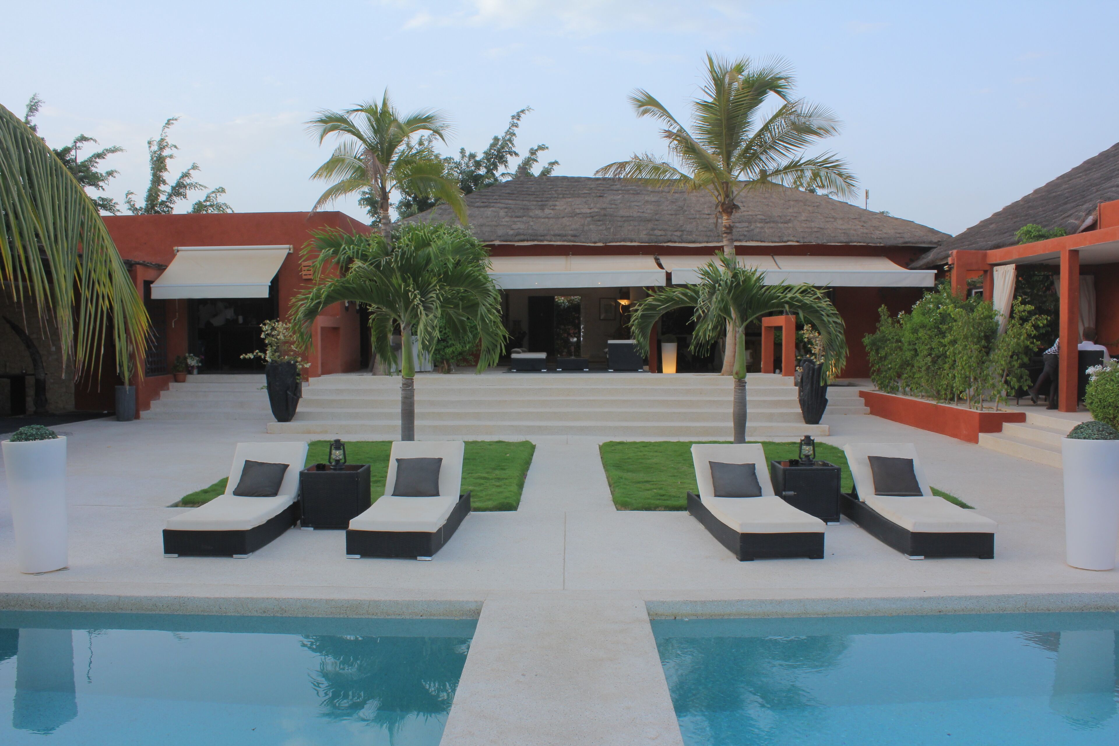 A poolside area with lounge chairs and a clear view of a building with a thatched roof.