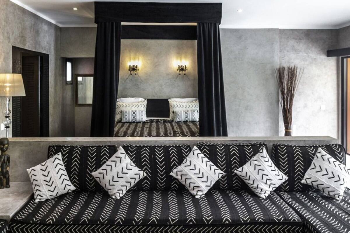 Ein modernes Hotelzimmer mit einem großen Bett, schwarz-weißen Kissen mit Muster, einer Couch und einem Spiegel.