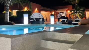 A swimming pool with steps leading up to it, surrounded by lounge chairs and palm trees.
