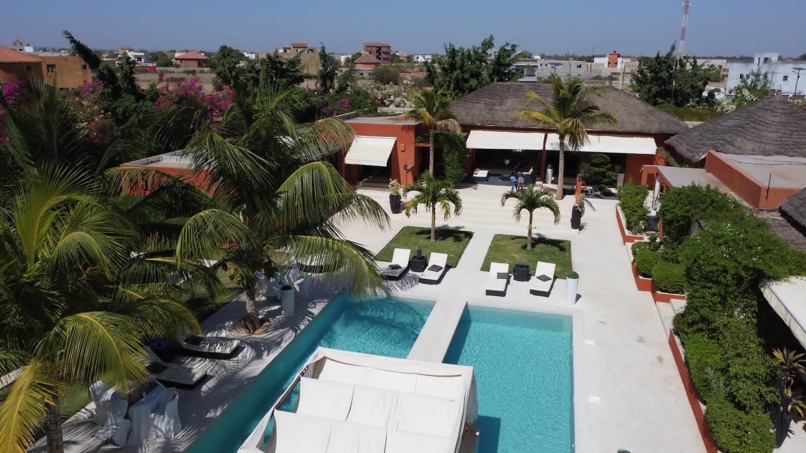 A resort with a central swimming pool, sun loungers, palm trees, and a view of the surrounding area.