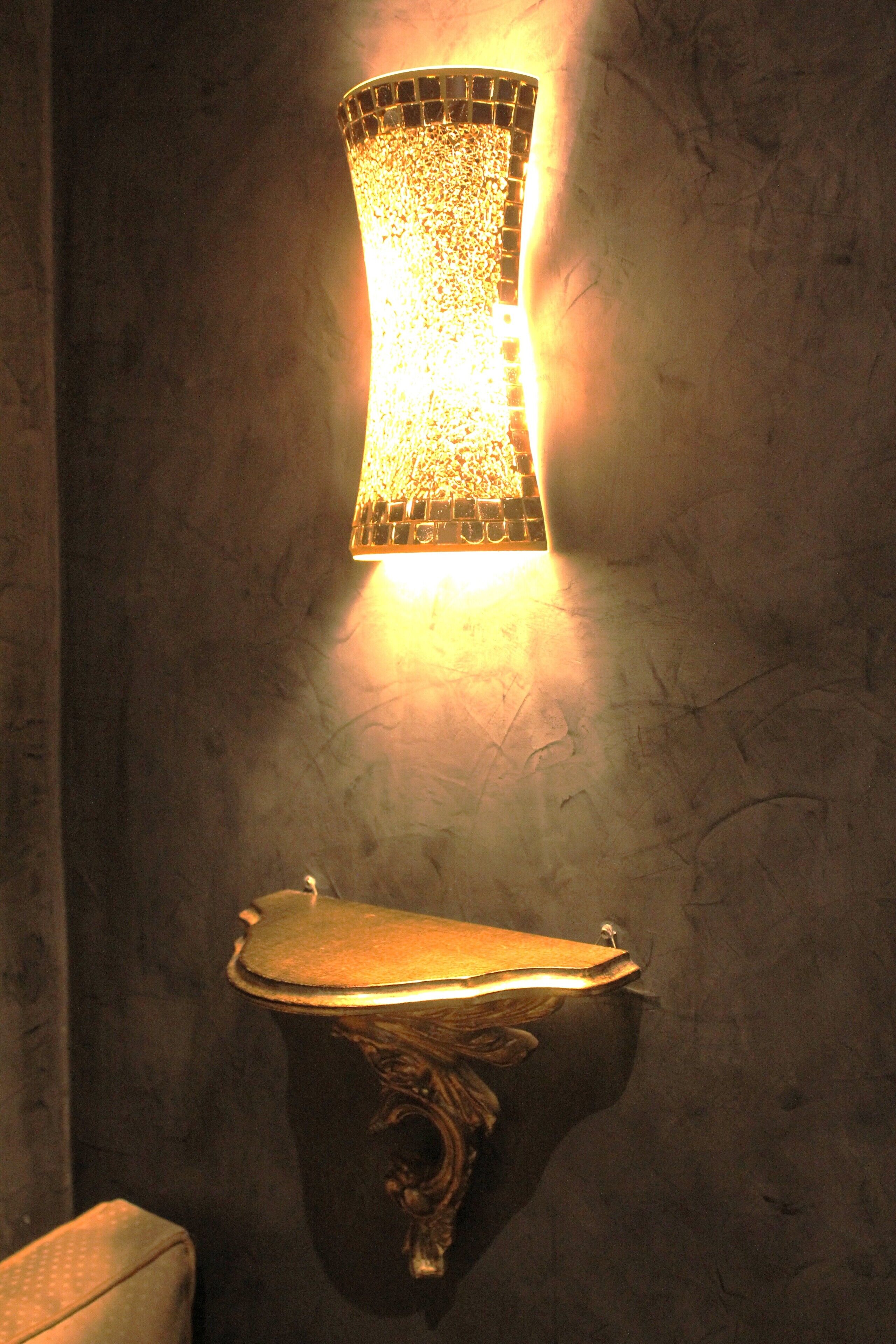 A wall-mounted light fixture with a mosaic design and a decorative wall-mounted toilet.
