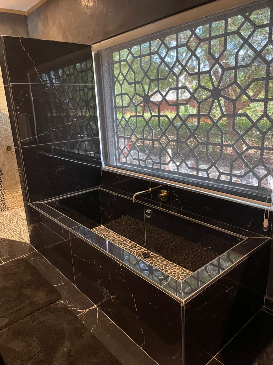 Un baño de mármol negro con cabina de ducha de vidrio y vistas a un jardín.