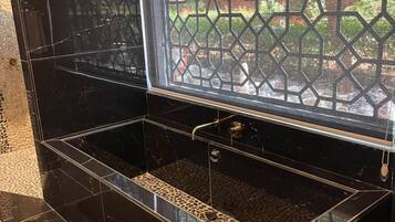 Un baño de mármol negro con cabina de ducha de vidrio y vistas a un jardín.
